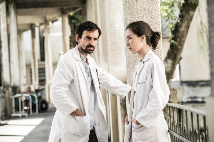 Personagens Evandro (à esquerda) e Carolina (à direita), vestidos de médico, no hospital do seriado Sob Pressão especial Covid