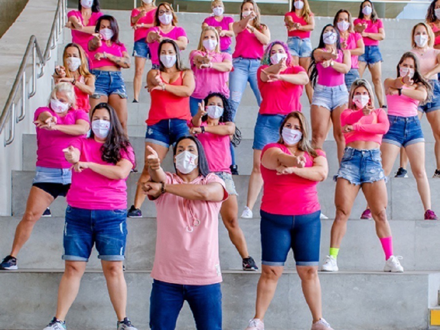 Grupo de pessoas vestidas de short jeans e blusa rosa dançando a coreografia de Me Gusta em uma escadaria