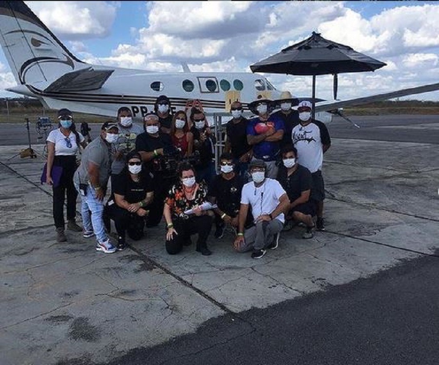 Grupo de elenco e produção de Bem-vinda a Quixeramobim em posando frente a um jatinho, todos usando mãscara