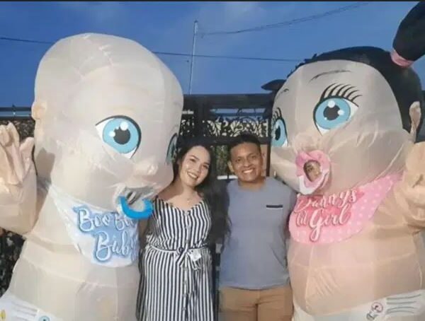 Imagem de um casal ao centro com duas pessoas vestidas como bebês gigantes, sendo um menino (esq.) e uma menina (dir), de um vídeo de um chá de revelação bizarro em que esses bonecosbrigam