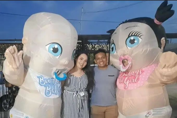 Imagem de um casal ao centro com duas pessoas vestidas como bebês gigantes, sendo um menino (esq.) e uma menina (dir), de um vídeo de um chá de revelação bizarro em que esses bonecosbrigam