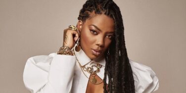 Ludmilla de roupa branca, com muitas correntes. Primeira mulher preta e latina com um bilhão de streamings