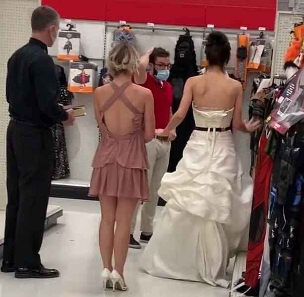 mulher vestida de noiva fazendo uma emboscada próximo a um funcionário da loja, supostamente o noivo, coçando a cabeça, um juiz de paz e uma dama de honra.
