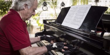 Maestro João Carlos Martins de blusa vermelha tocando piano com as luvas biônicas