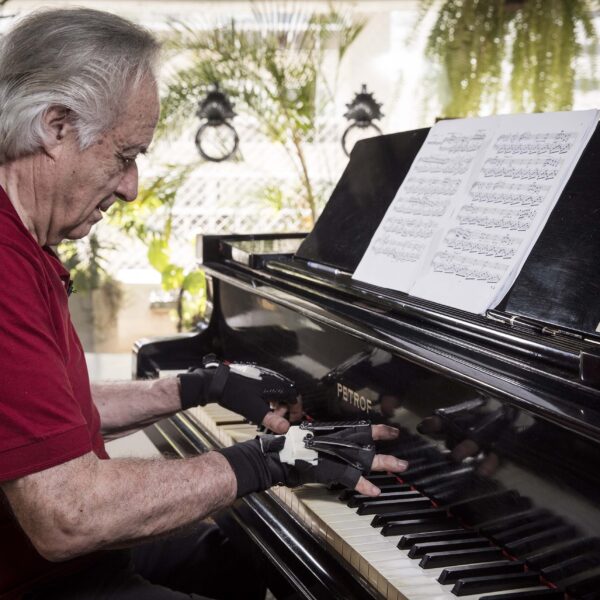 Maestro João Carlos Martins de blusa vermelha tocando piano com as luvas biônicas