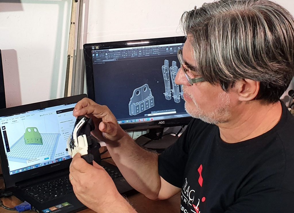 Designer que criou a luva biônica segurando sua invenção com um computador ao fundo