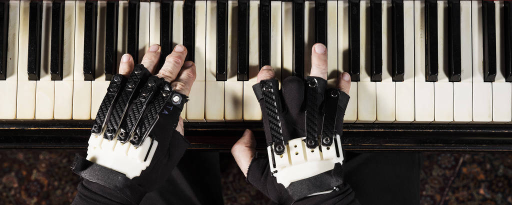 mãos do maestro João Carlos Martins com as luvas biônicas sobre um piano
